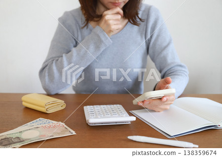 一位女士一邊看著智慧型手機一邊記錄家庭開支。 一位女士一邊看著智慧型手機一邊記錄家庭開支。 138359674