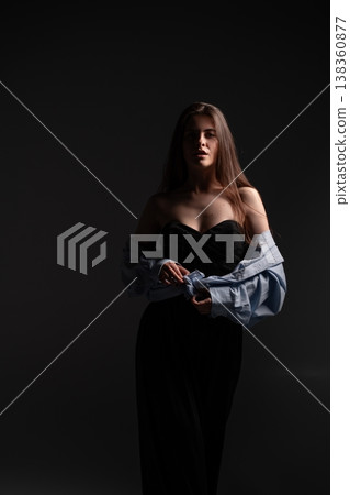 Young woman posing gracefully in a studio with strong chiaroscuro lighting, highlighting her features and fashionable attire, bringing a sense of elegance and moody ambiance Young woman posing gracefully in a studio with strong chiaroscuro lighting, highlighting her features and fashionable attire, bringing a sense of elegance and moody ambiance 138360877