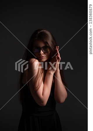 Woman posing wearing glasses, hands held together by face, creating a mysterious and thoughtful mood with soft light and shadow on a dark background Woman posing wearing glasses, hands held together by face, creating a mysterious and thoughtful mood with soft light and shadow on a dark background 138360879