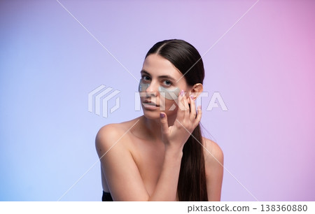 Young woman applying under-eye gel patches in pastel studio, promoting hydrated, dewy skin and self-care routine for depuffing, rejuvenation and fresh, radiant complexion Young woman applying under-eye gel patches in pastel studio, promoting hydrated, dewy skin and self-care routine for depuffing, rejuvenation and fresh, radiant complexion 138360880