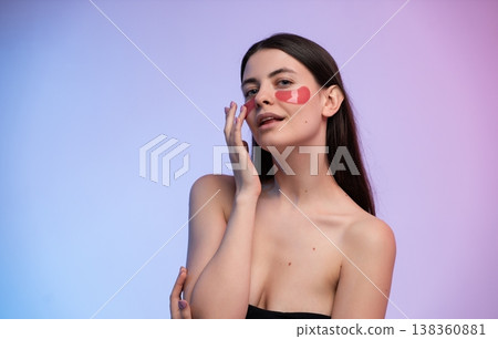 Young woman applying red eye patches on her face, embracing a self-care beauty routine for wellness and healthy glowing skin, standing against a colorful background Young woman applying red eye patches on her face, embracing a self-care beauty routine for wellness and healthy glowing skin, standing against a colorful background 138360881