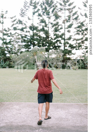 Man in red shirt walking toward nature field from bridge rear view Man in red shirt walking toward nature field from bridge rear view 138360995