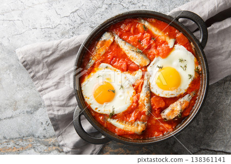 Homemade fried eggs with sardines in spicy tomato sauce close-up in a frying pan. Horizontal top view Homemade fried eggs with sardines in spicy tomato sauce close-up in a frying pan. Horizontal top view 138361141