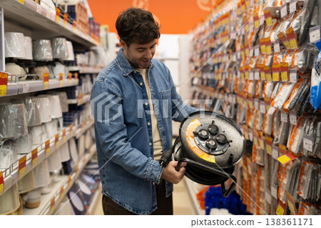 Man holding an extension cord reel, shopping for electrical equipment in a hardware store 138361171