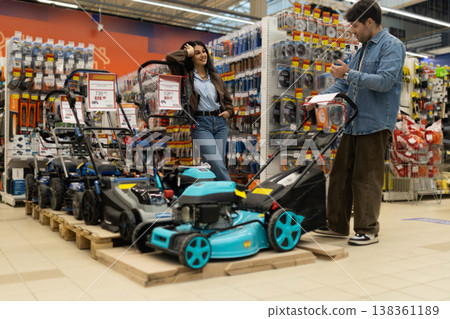 Couple selecting a new lawn mower from a variety of models in a large retail store Couple selecting a new lawn mower from a variety of models in a large retail store 138361189