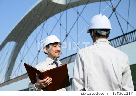 Japanese men in work clothes having a meeting with a bridge in the background. 138361217