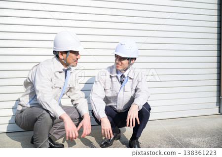 A Japanese man in work clothes sits and talks in front of a shutter. 138361223