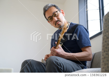 A Japanese man practicing guitar in his room. 138361228