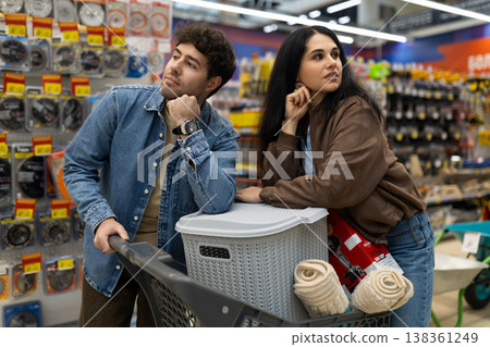 Couple pushing shopping cart and thinking about options in a brightly lit hardware store aisle Couple pushing shopping cart and thinking about options in a brightly lit hardware store aisle 138361249
