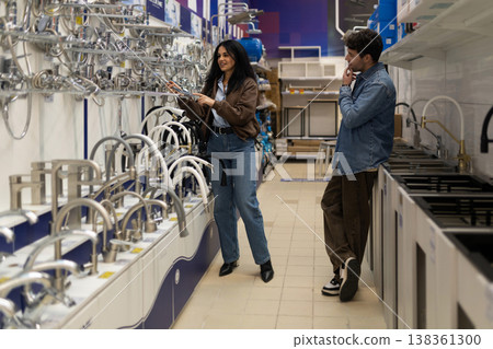 Couple shopping for plumbing fixtures, looking at different faucets in a home improvement store Couple shopping for plumbing fixtures, looking at different faucets in a home improvement store 138361300