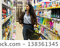 Woman holding a shopping basket while choosing products from shelves in a grocery store 138361345