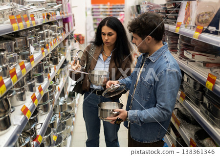 Young couple comparing stainless steel pots and selecting kitchen utensils at a store Young couple comparing stainless steel pots and selecting kitchen utensils at a store 138361346