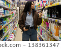 Woman holding product, considering options in a crowded retail store aisle 138361347