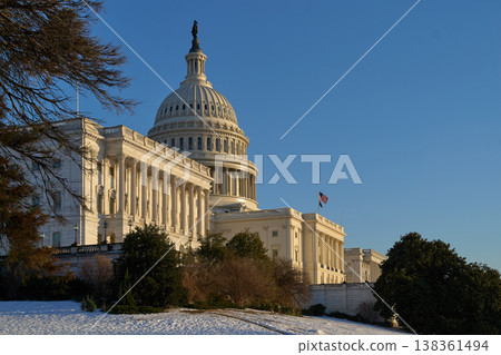 Last beams of golden sunlight on the United States Capitol Building in Washington, DC, with the American flag waving, blue sky backrgound Last beams of golden sunlight on the United States Capitol Building in Washington, DC, with the American flag waving, blue sky backrgound 138361494