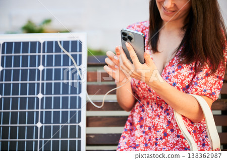 Cropped view of happy women using smartphone connected to solar panel. Integration of sustainable renewable energy into everyday life, demonstrating practical use of solar power for charging devices. 138362987