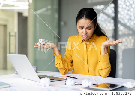 Stressed businesswoman dealing with an office problem, holding crumpled paper and showing frustration while sitting at her desk with a laptop and documents Stressed businesswoman dealing with an office problem, holding crumpled paper and showing frustration while sitting at her desk with a laptop and documents 138363272