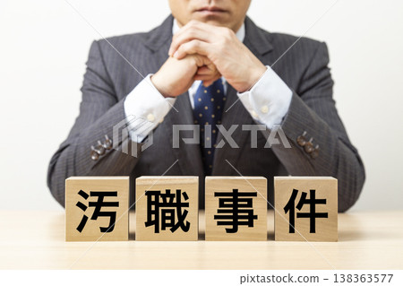 一塊寫著「腐敗醜聞」字樣的磚塊和一個商人 一塊寫著「腐敗醜聞」字樣的磚塊和一個商人 138363577