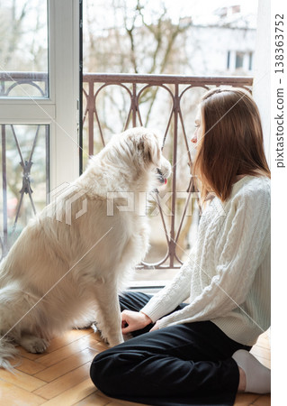Woman and golden retriever dog sitting by balcony door Woman and golden retriever dog sitting by balcony door 138363752