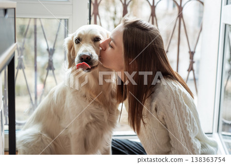 Woman kissing loving golden retriever dog indoors 138363754