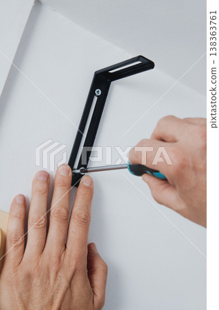 a man fastening a screw in a wall bracket 138363761
