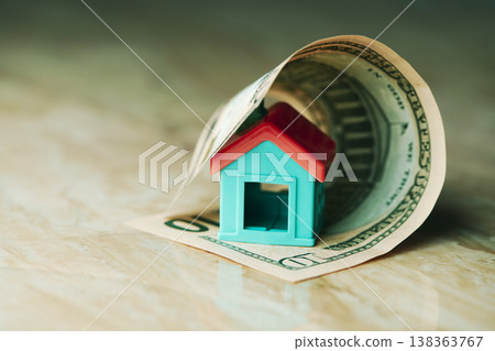 a toy house enclosed by a rolled dollar bill a toy house enclosed by a rolled dollar bill 138363767