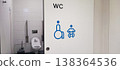 An accessible public restroom with wheelchair and baby changing symbols on the door and safety grab bars inside. Concepts of inclusivity, accessibility, and modern public infrastructure design. 138364536
