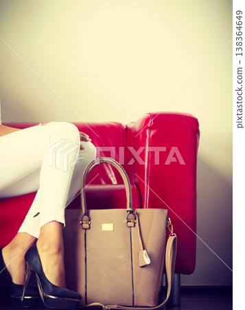 Woman sitting on sofa presenting leather bag Woman sitting on sofa presenting leather bag 138364649