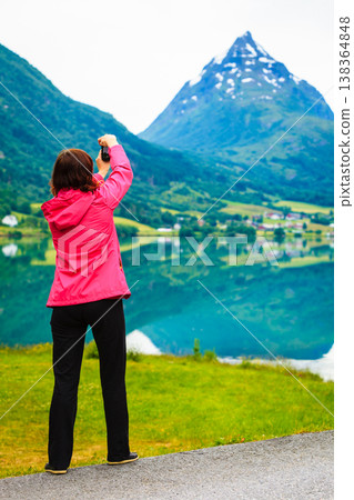 Tourist taking photo at norwegian fjord lake Tourist taking photo at norwegian fjord lake 138364848