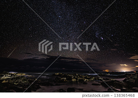 A night sea illuminated by shooting stars: A fantastical scene of reefs and starry sky. A night sea illuminated by shooting stars: A fantastical scene of reefs and starry sky. 138365468