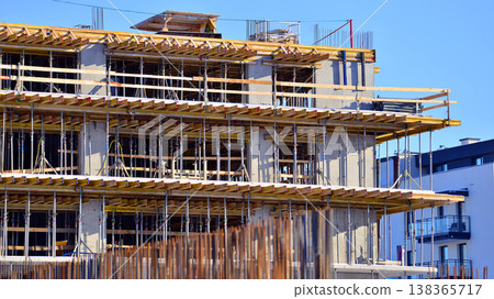 Building under construction against a blue sky background. Builders work on large construction sites. Exterior view of under construction building with modern design under construction. Building under construction against a blue sky background. Builders work on large construction sites. Exterior view of under construction building with modern design under construction. 138365717