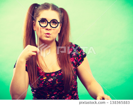 Happy teenage woman holding fake eyeglasses on stick Happy teenage woman holding fake eyeglasses on stick 138365883