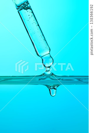 Pipette dripping clear liquid into blue water 138366192