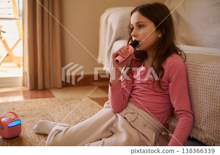 Young Girl Singing Into Handheld Microphone At Home With Pink Portable Speaker Young Girl Singing Into Handheld Microphone At Home With Pink Portable Speaker 138366339
