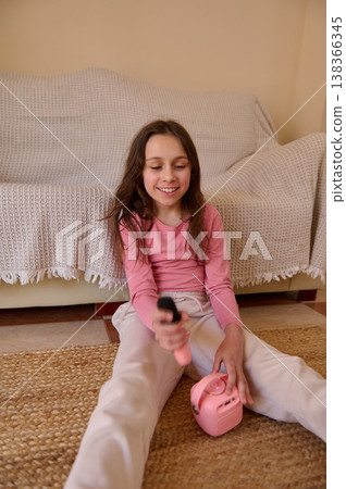 Smiling Girl Playing With Pink Toy Speaker At Home Sitting On Rug With Remote Control Smiling Girl Playing With Pink Toy Speaker At Home Sitting On Rug With Remote Control 138366345