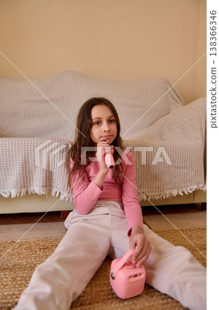 Young Girl Singing with Pink Microphone and Portable Speaker in Cozy Living Room Young Girl Singing with Pink Microphone and Portable Speaker in Cozy Living Room 138366346