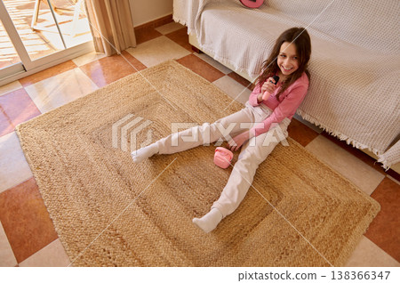 Smiling Girl Singing With Toy Microphone on Rug in Cozy Living Room Smiling Girl Singing With Toy Microphone on Rug in Cozy Living Room 138366347