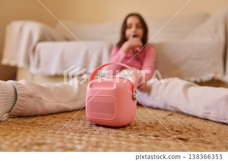 Young Girl Listening To A Pink Portable Speaker While Singing At Home In A Cozy Living Room Young Girl Listening To A Pink Portable Speaker While Singing At Home In A Cozy Living Room 138366353