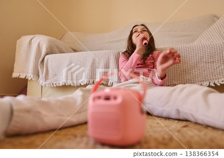 Young Girl Singing Into Toy Microphone While Relaxing On Living Room Floor With Pink Speaker 138366354
