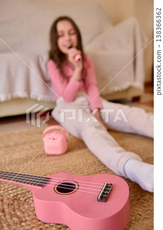 Young Girl Singing With Pink Ukulele At Home On Rug, Playful Childhood Music Time Young Girl Singing With Pink Ukulele At Home On Rug, Playful Childhood Music Time 138366362