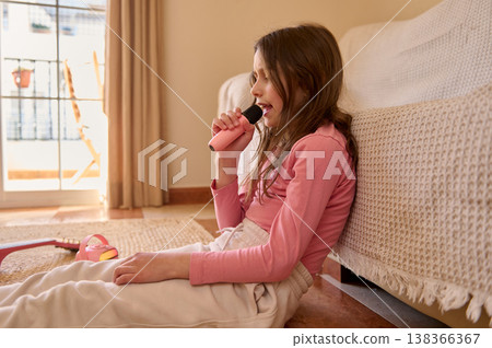 Young Girl Singing Into Toy Microphone at Home in Cozy Living Room Young Girl Singing Into Toy Microphone at Home in Cozy Living Room 138366367