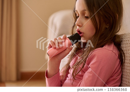 Girl Singing into Pink Microphone While Sitting on Sofa at Home Girl Singing into Pink Microphone While Sitting on Sofa at Home 138366368