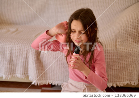 Young Girl Singing With Microphone On Sofa At Home Playing Music And Pretend Performance Young Girl Singing With Microphone On Sofa At Home Playing Music And Pretend Performance 138366369