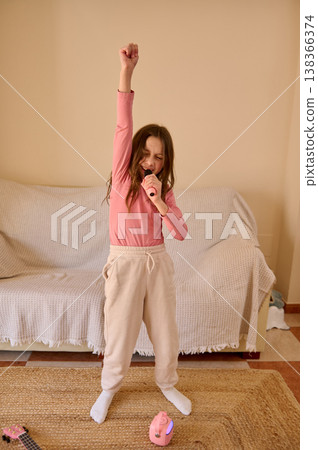 Young Girl Singing at Home With Microphone and Raised Arm in Living Room Performance 138366374