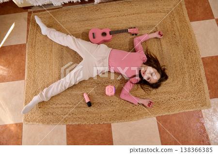 Young Girl Lying On Rug With Pink Ukulele And Toys Relaxing In Cozy Home Interior Young Girl Lying On Rug With Pink Ukulele And Toys Relaxing In Cozy Home Interior 138366385