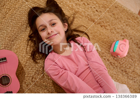 Smiling Little Girl Lying on Rug With Pink Ukulele and Portable Speaker Smiling Little Girl Lying on Rug With Pink Ukulele and Portable Speaker 138366389