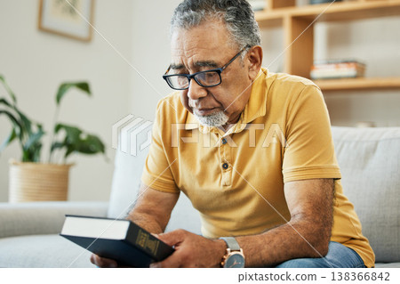Man, holding and book in thought at home, memory and alone for comfort in hope. Male, person or grandfather on sofa in living room with thoughts of bible, religion or church in prayer for support Man, holding and book in thought at home, memory and alone for comfort in hope. Male, person or grandfather on sofa in living room with thoughts of bible, religion or church in prayer for support 138366842