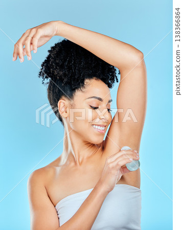 Smile, beauty and underarm deodorant with a woman on a blue background in studio for hygiene. Skincare, product and fresh with a happy young person looking to apply a scent or fragrance to her armpit 138366864