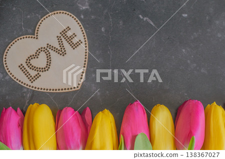 Vibrant yellow and pink tulips in a row on dark marble with a wooden LOVE heart. High-contrast Dark Moody composition with premium textures and large copy space Vibrant yellow and pink tulips in a row on dark marble with a wooden LOVE heart. High-contrast Dark Moody composition with premium textures and large copy space 138367027