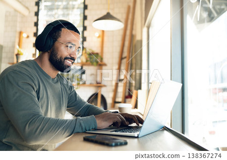 Man, remote work and laptop in coffee shop, headphones and productivity with freelancer and copywriter, writing article and blog. Workflow, typing on pc in cafe and copywriting, music and research 138367274
