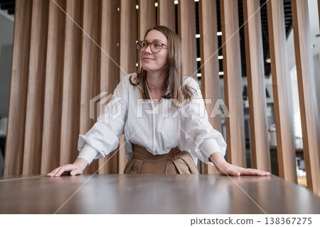Young woman with glasses smiling at desk in modern office with wood panel wall. Smiling, glasses, desk, office, young woman, panel wall. Young woman with glasses smiling at desk in modern office with wood panel wall. Smiling, glasses, desk, office, young woman, panel wall. 138367275